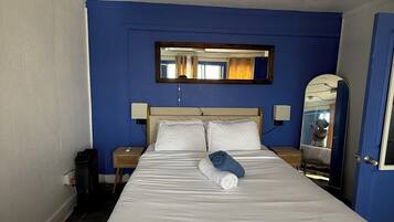Une chambre d’hôtel avec un grand lit, deux tables de chevet, un miroir et une fenêtre avec des rideaux.