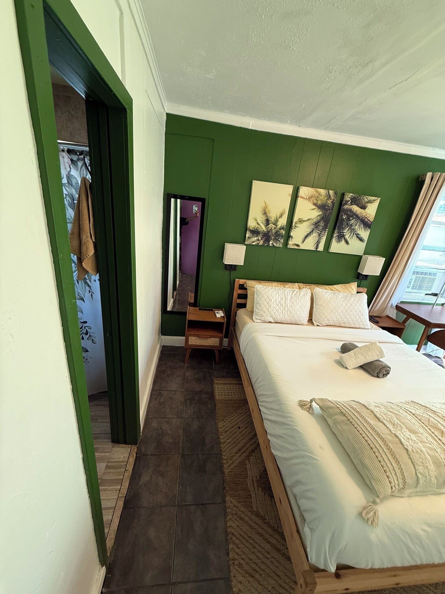 Een slaapkamer met een bed, nachtkastje, spiegel en een deur naar een andere kamer.