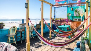 Una terraza de madera con una hamaca, sillas y una mesa.