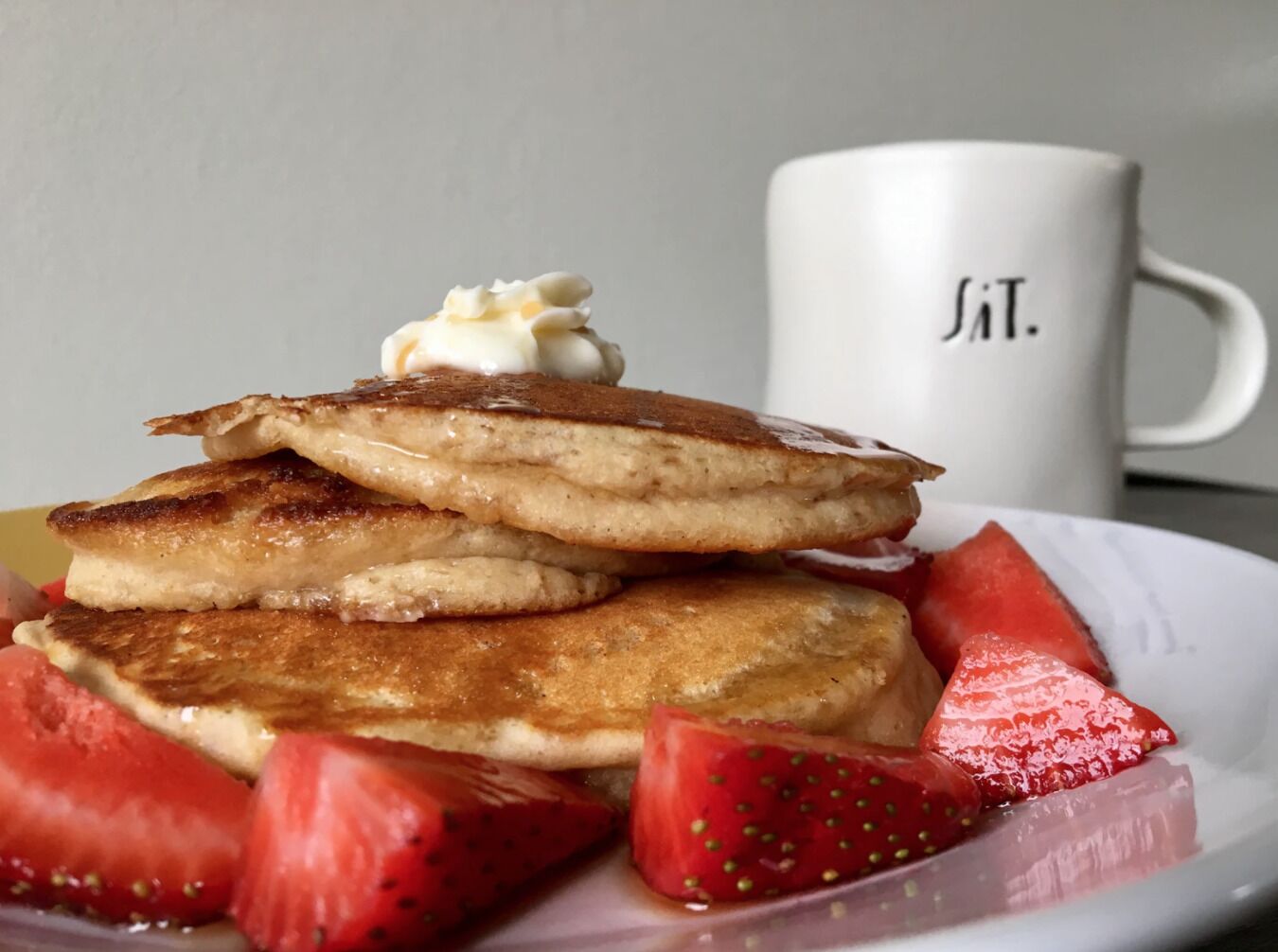 Una pila de panqueques con jarabe y crema batida, acompañada de fresas en rodajas y sandía en un plato.