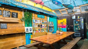 Interior de madera con una mesa y bancos de madera, una máquina expendedora y un mural colorido en la pared.