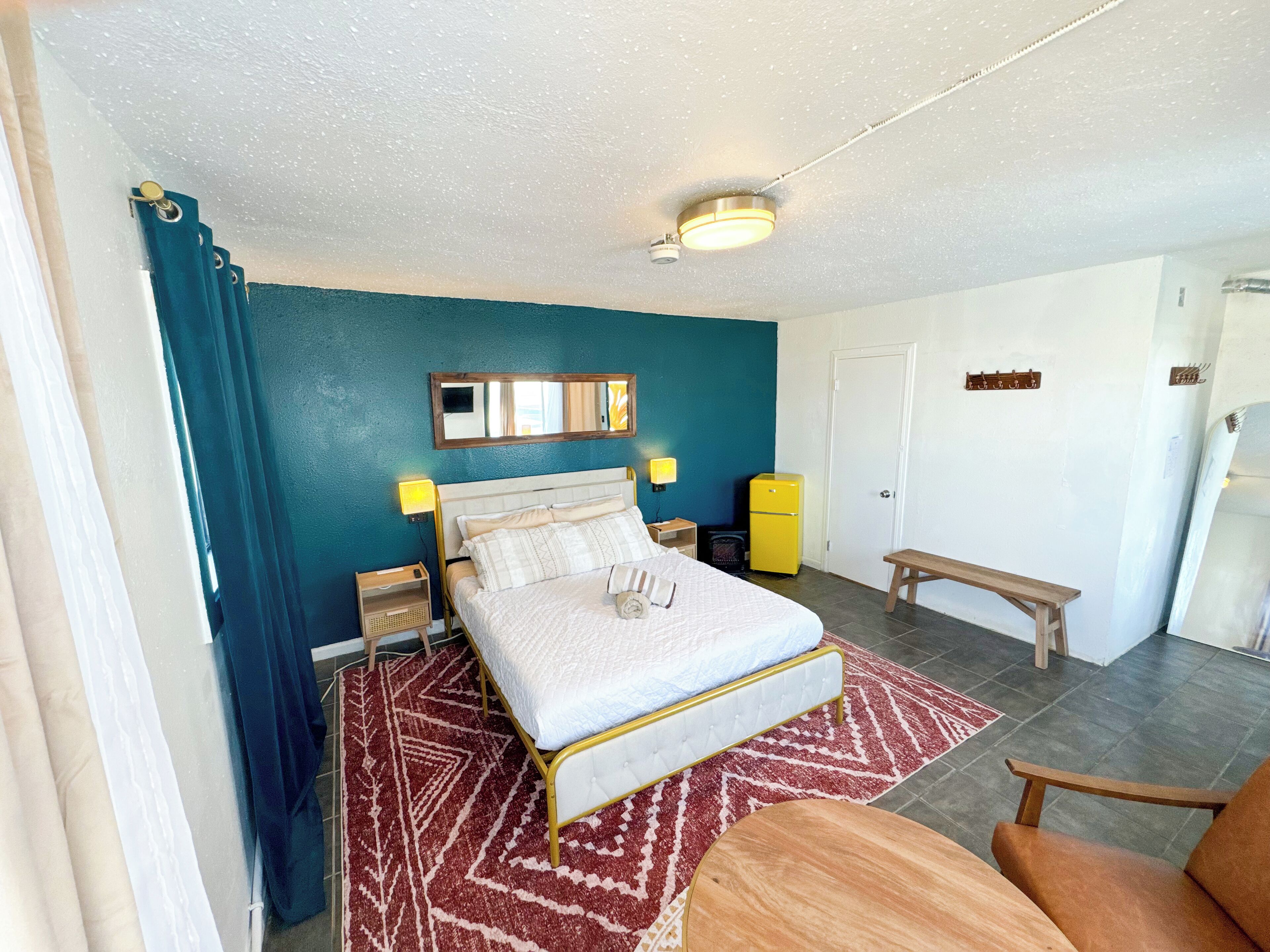 Une chambre à coucher comprenant un lit, des tables de chevet, un banc, un miroir et un réfrigérateur.