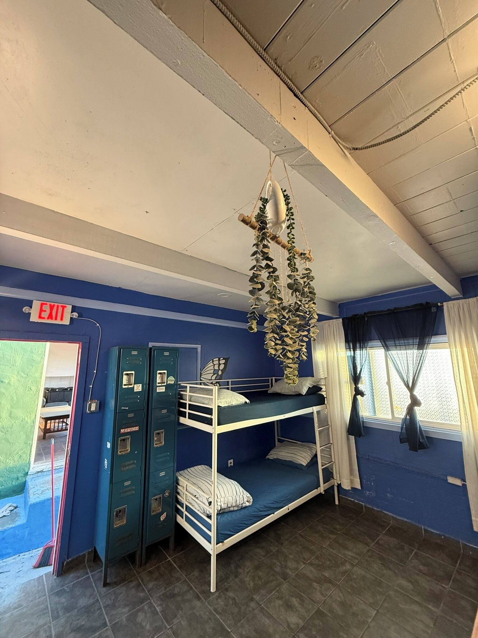 A bunk bed room with a hanging plant, lockers, and an exit sign.