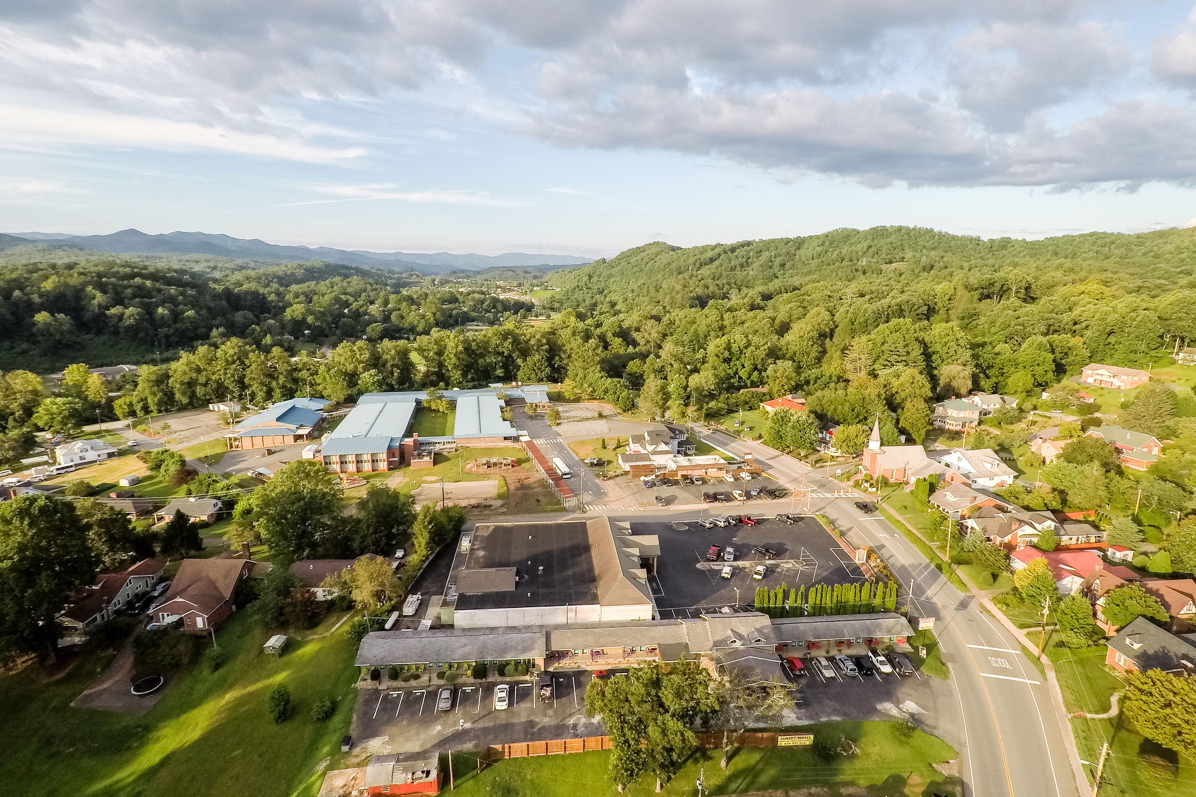 An aerial view of a town with a large industrial area, residential houses, and green hills in the background.