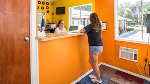 A reception area with a wooden counter, a computer, and a window with a view of the outside. - Sunset Motel (Murphy)