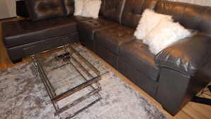 A sectional sofa with white fluffy pillows, a glass coffee table, and a shaggy rug. - Sunset Motel (Murphy)