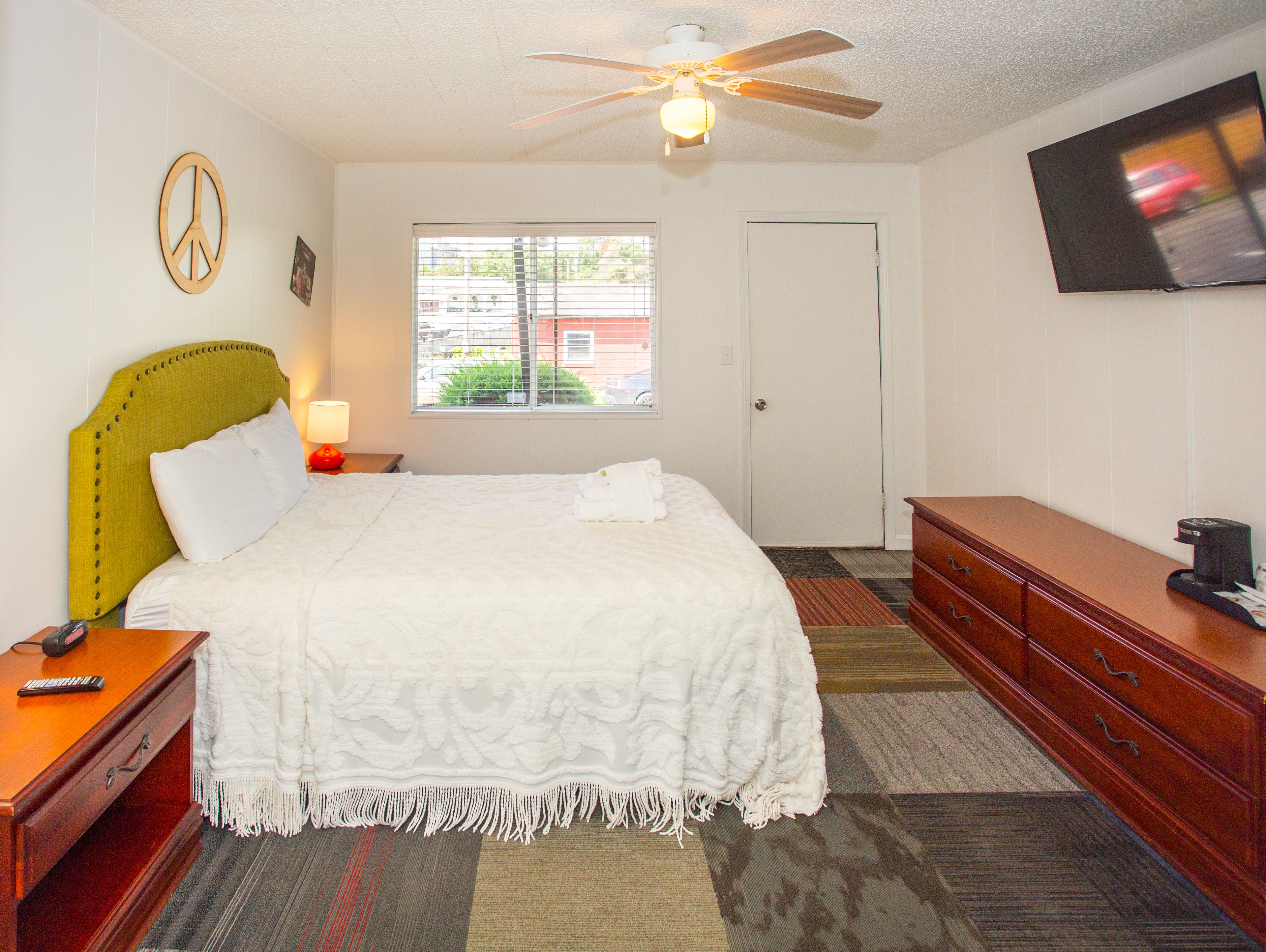 Habitación de hotel con cama, escritorio, cómoda, televisor, ventilador de techo, ventana y puerta.
