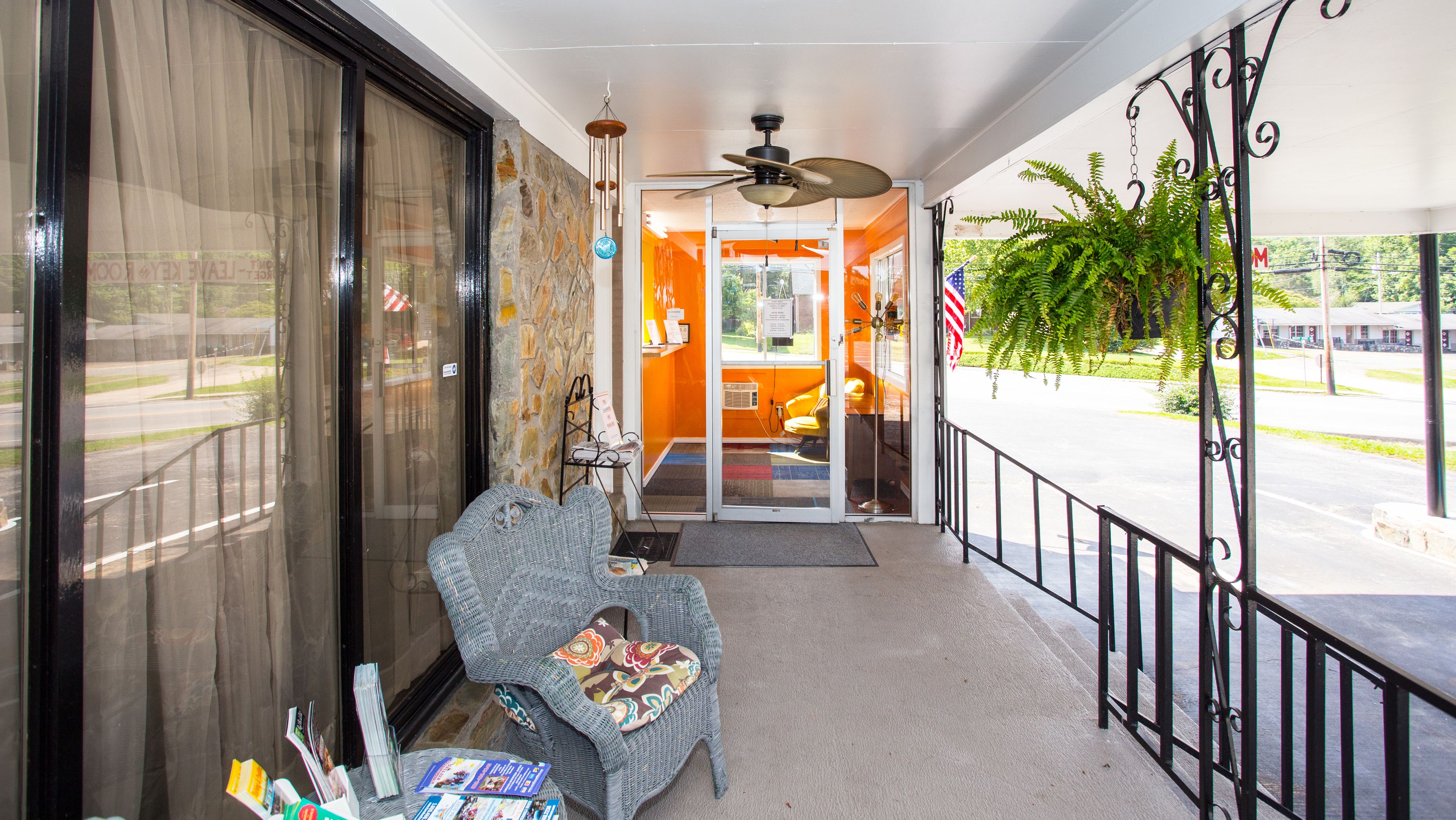 A covered porch with a wicker chair, a small table with magazines, and a view of the street.