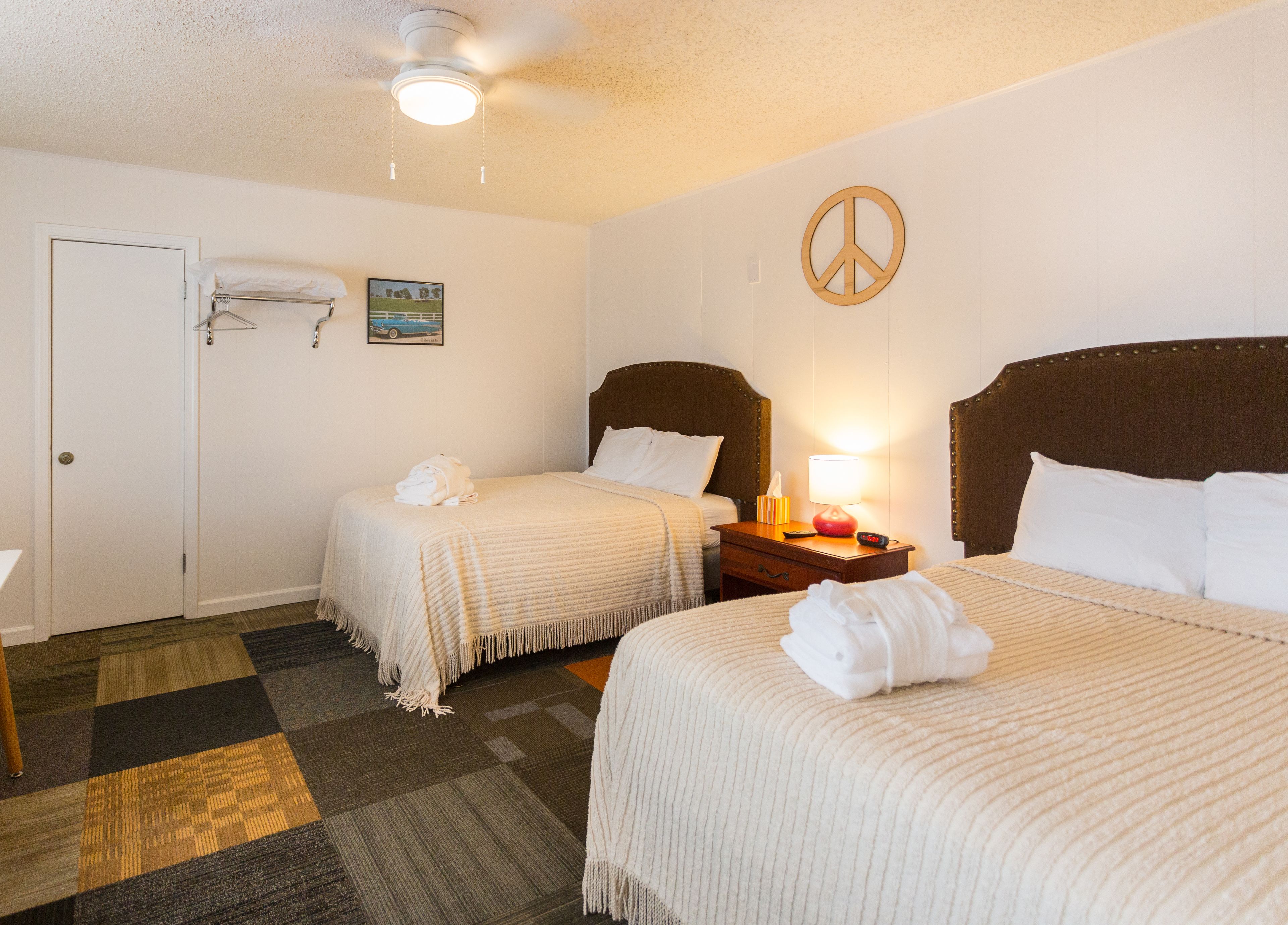 A hotel room with two beds, a ceiling fan, a peace symbol on the wall, and a painting.
