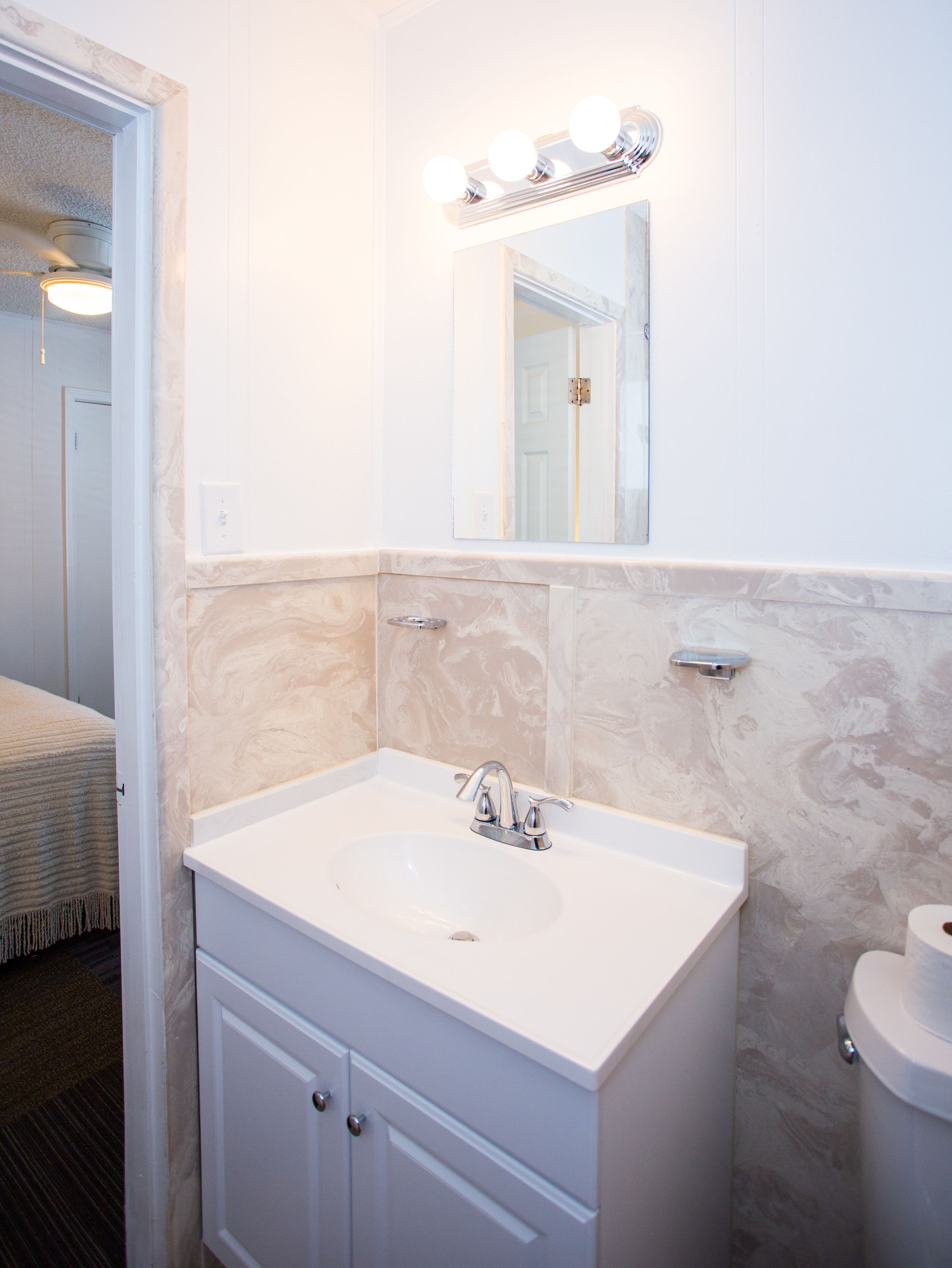 Une salle de bain avec un lavabo, un meuble-lavabo et un miroir blancs. On peut voir des toilettes sur la droite.