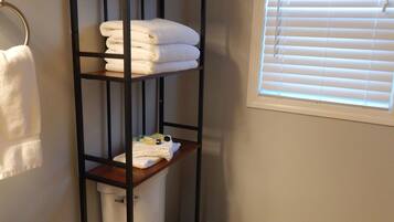 A bathroom with a toilet, a shelf with folded towels, and a window with blinds.