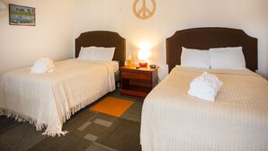 A hotel room with two single beds, a wooden headboard, a peace sign decoration, a nightstand with a lamp, and a framed picture on the wall.