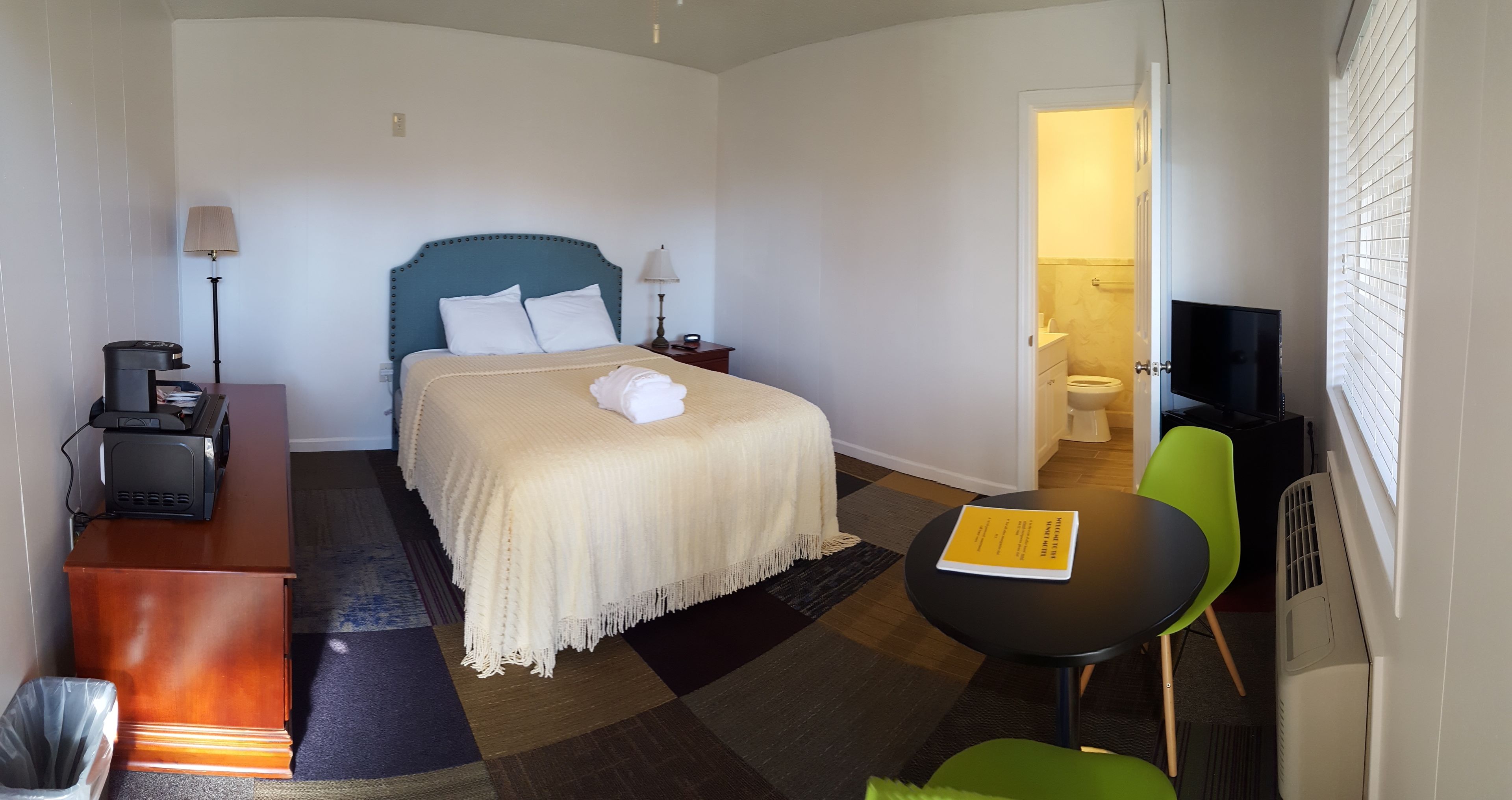 A hotel room with a bed, bedside table, lamp, chair, and a small table with a book.