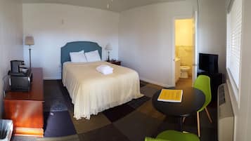 A hotel room with a bed, bedside table, lamp, chair, and a small table with a book.