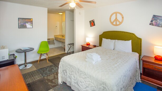 A hotel room with a bed, a desk, a chair, a bathroom, and a ceiling fan.