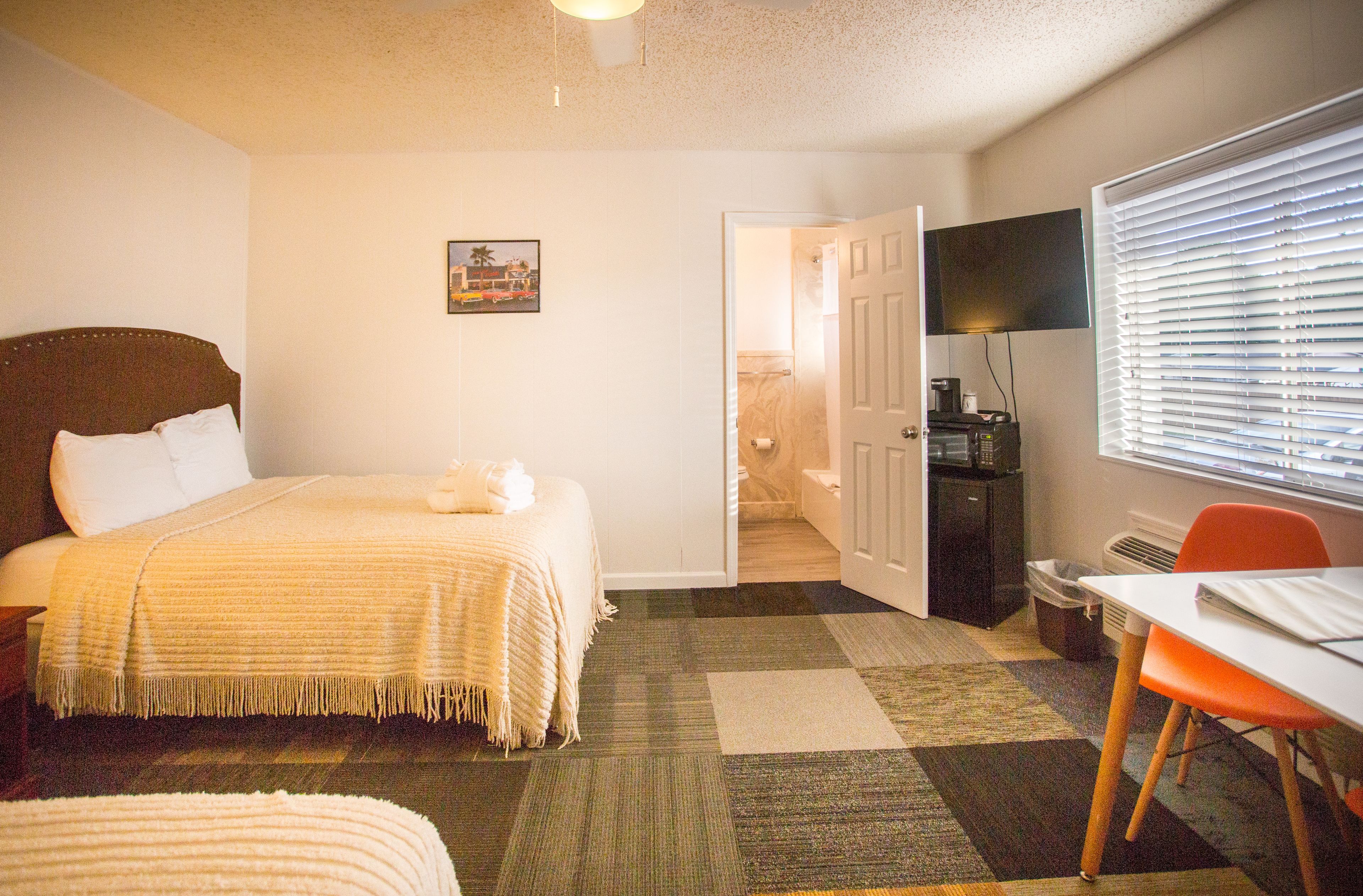 A hotel room with a bed, a desk, a chair, a TV, and a window with blinds.