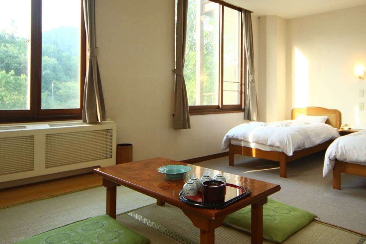 Une chambre d’hôtel avec deux lits, une table avec un service à thé et une vue sur la verdure par la fenêtre.