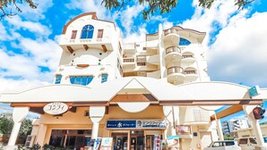 A multi-story hotel with a distinctive architectural design, featuring balconies and a covered entrance. - ALL FRIENDS - Hostel (Nago)