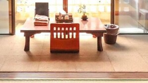 A traditional Japanese tatami mat room with a low table, a wooden chair, and a small potted plant. - ALL FRIENDS - Hostel (Nago)