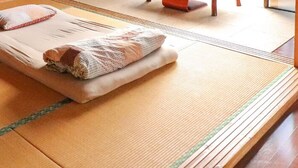 A tatami mat room with a futon bed, a pillow, and a small wooden stool. - ALL FRIENDS - Hostel (Nago)