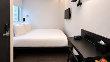 Ein kleines Hotelzimmer mit Bett, Schreibtisch, Stuhl, Fernseher und Fenster.
