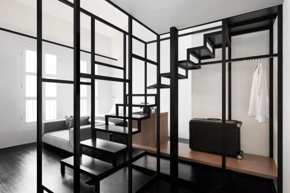 Een moderne kamer met een zwart geometrisch tussenschot, een trap, een zithoek en een koffer op een plank.