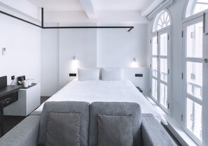 A modern hotel room with a large bed, bedside tables, and a desk with a chair. There are large windows with arched tops and a view of the outside. - Hotel Mono (Singapore)