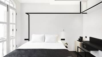 A modern hotel room with a large bed, a desk, and a window with blinds.