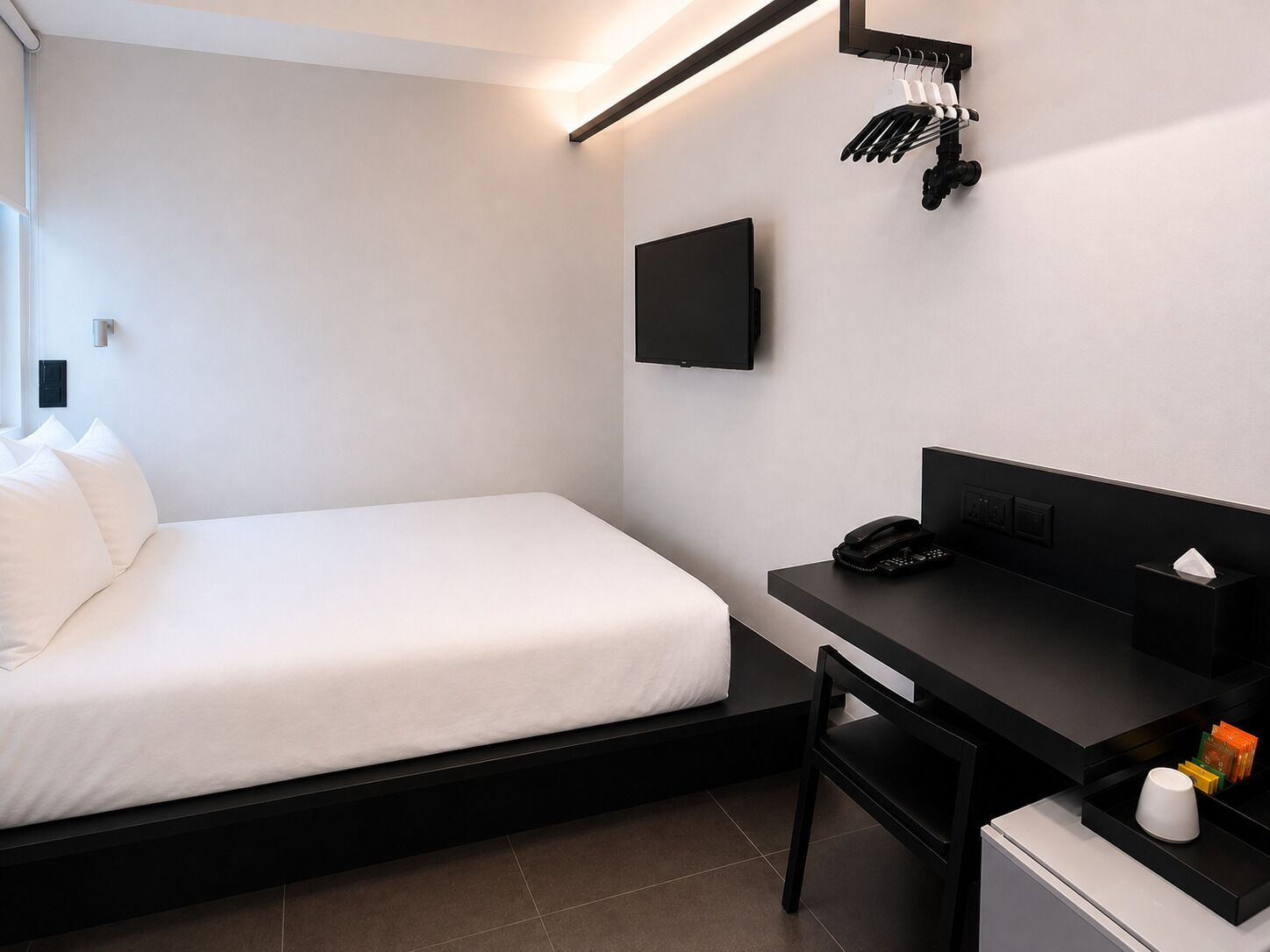A hotel room with a bed, a desk, a chair, a flat-screen TV, a telephone, and a small table with a tissue box and a cup.