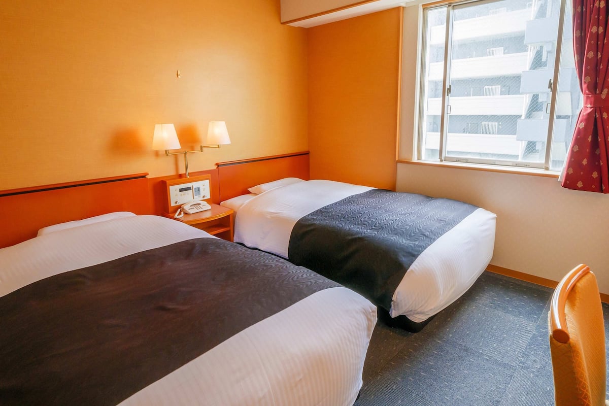 A hotel room with two beds, a nightstand with a phone, and a window with curtains.