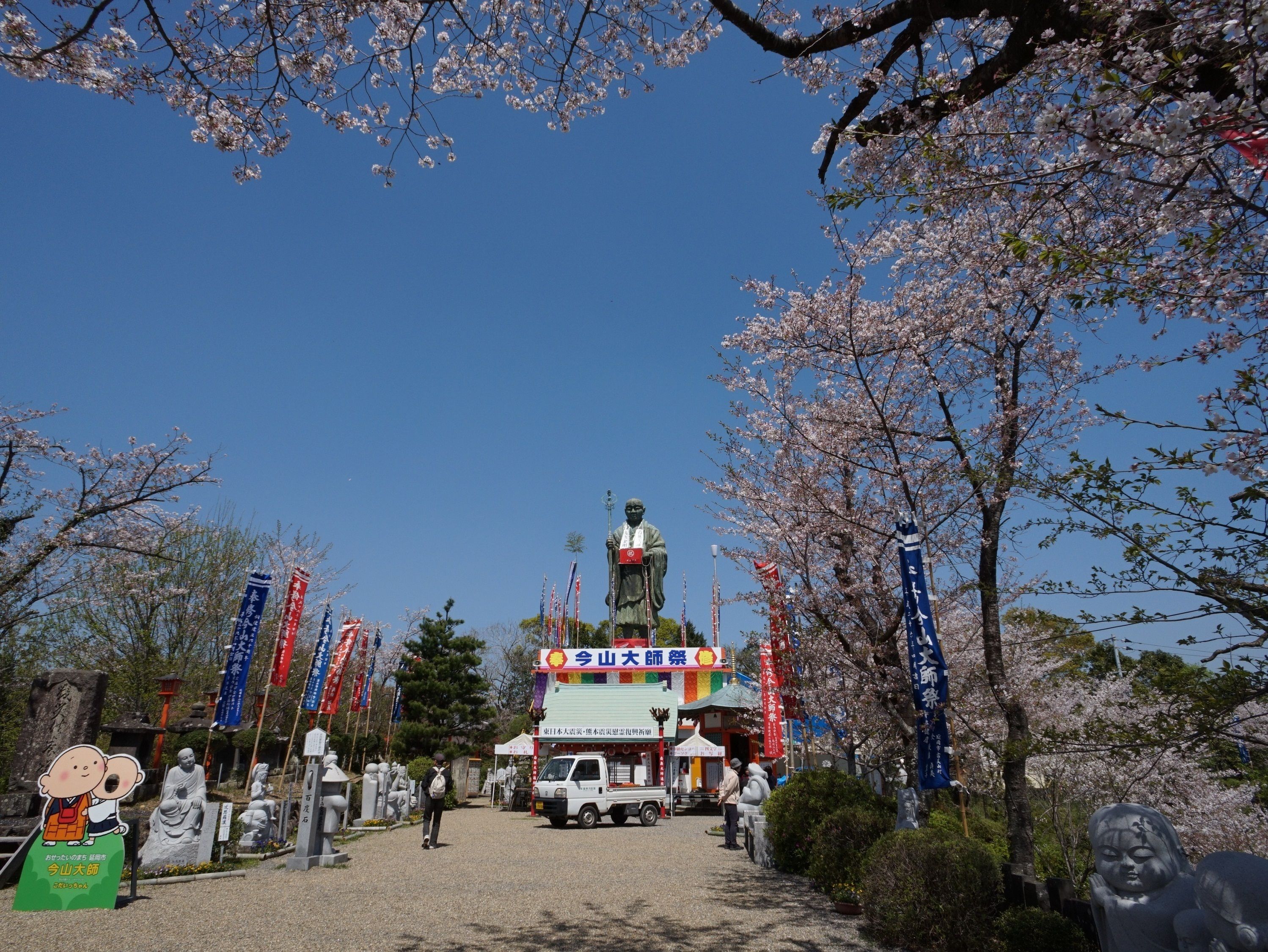 A shrine with a statue, surrounded by cherry blossoms and flags.