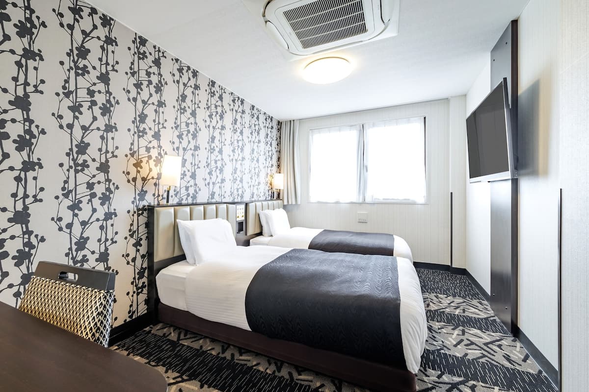 A hotel room with two beds, a TV, a ceiling fan, and a large window.