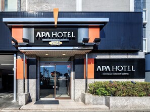 Exterior de l'APA Hotel amb un disseny modern, que destaca una entrada ben visible i un senyal clar amb el nom i l'adreça de l'hotel.