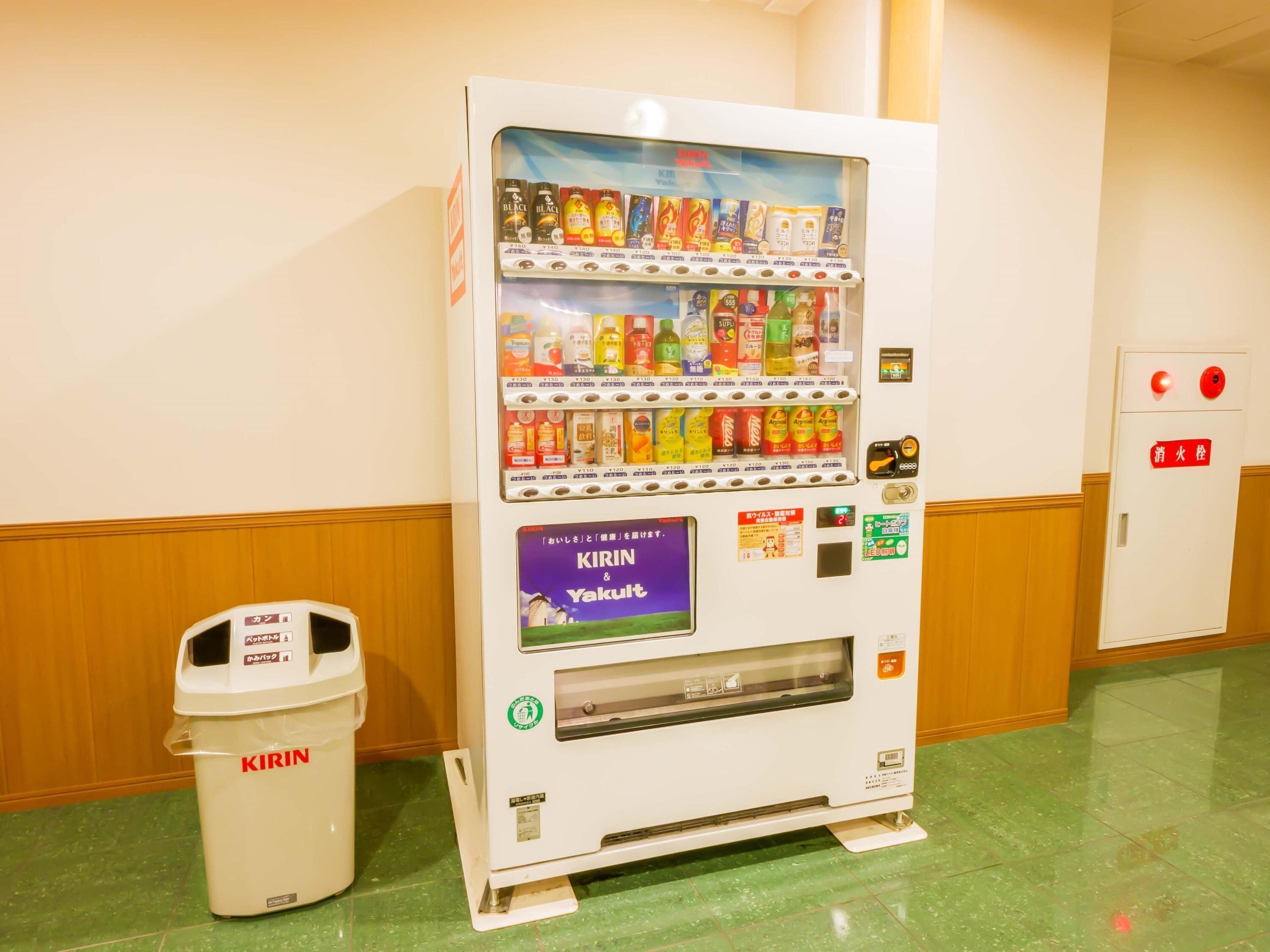 A vending machine with various beverages and snacks, a trash bin labeled 'KIRIN', and a door with emergency exit signs.