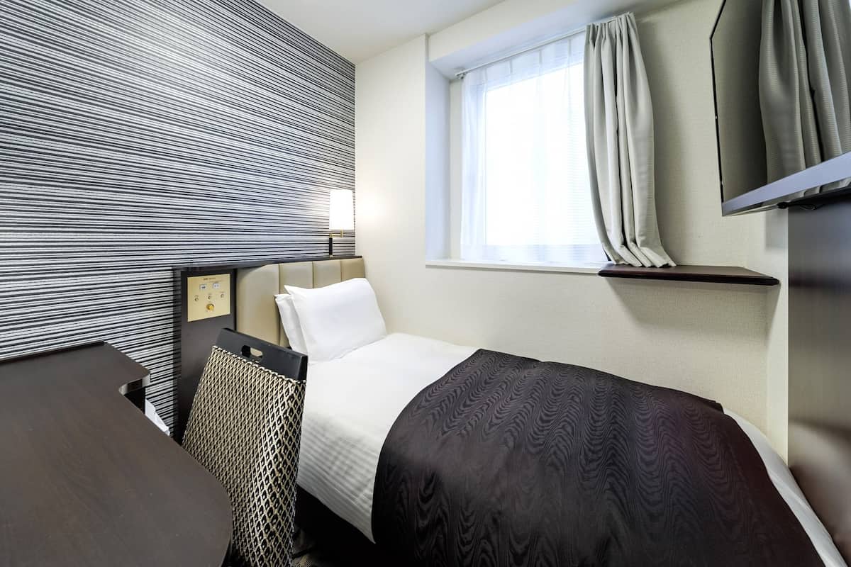 A hotel room with a bed, a desk, a chair, a TV, a window with curtains, and a wall with a striped pattern.