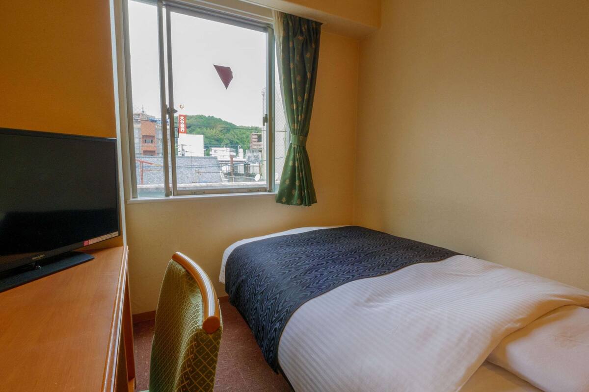 A hotel room with a bed, a TV, and a window with curtains.