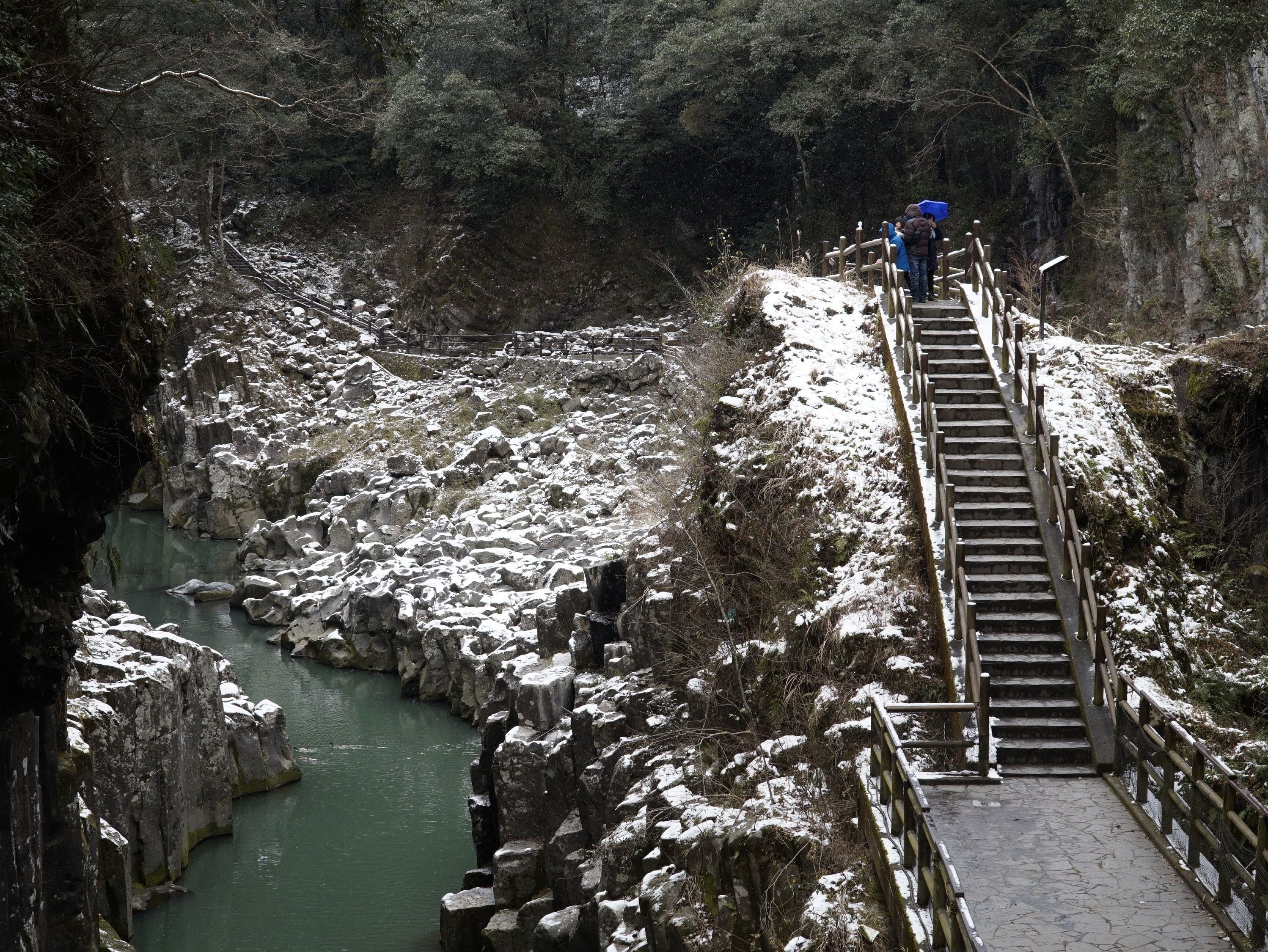 A wooden staircase leading down to a river surrounded by rocky terrain and sparse vegetation.