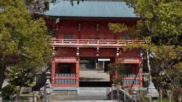 Un bâtiment traditionnel japonais, avec une façade rouge et un toit vert, entouré d’arbres et surplombant un pont de pierre.