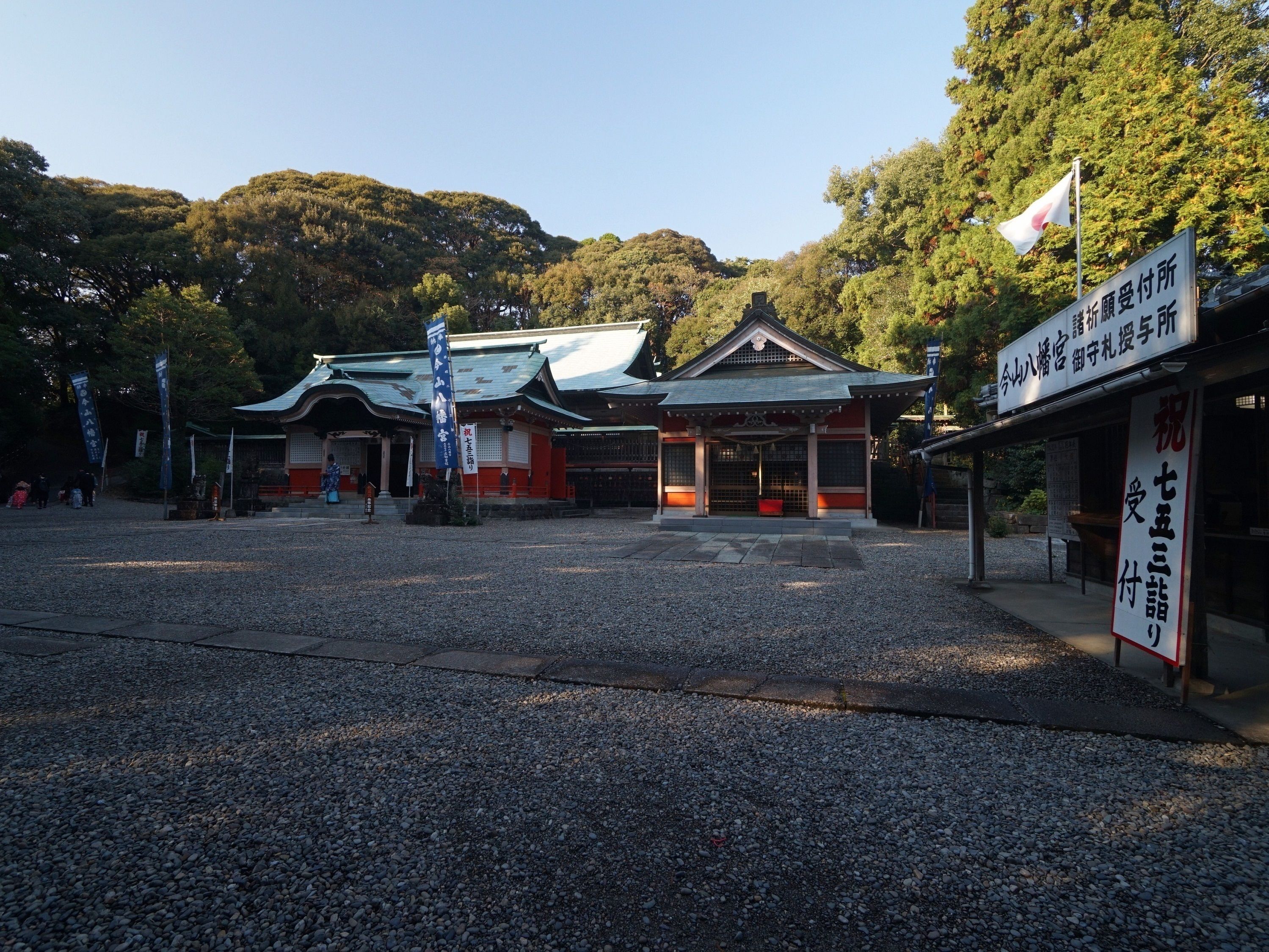 A traditional Japanese building with a tiled roof and wooden structure, surrounded by gravel and trees.