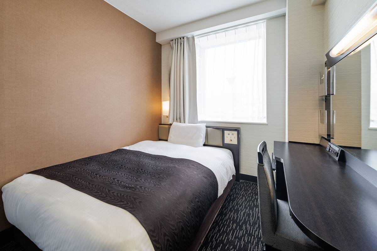 A hotel room with a bed, a desk, and a window with curtains.
