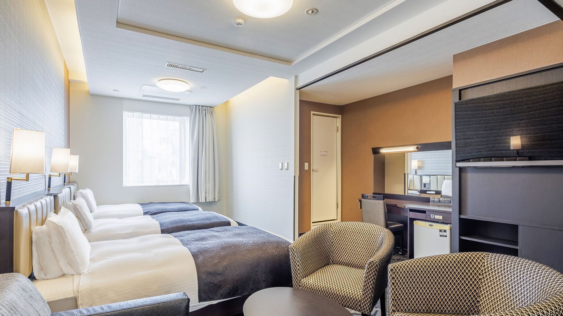 A hotel room with a bed, two bedside tables with lamps, a desk with a chair, a mirror, and a wardrobe.