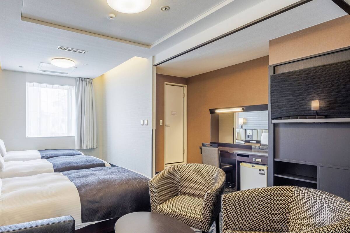 A hotel room with a bed, two bedside tables with lamps, a desk with a chair, a mirror, and a wardrobe.
