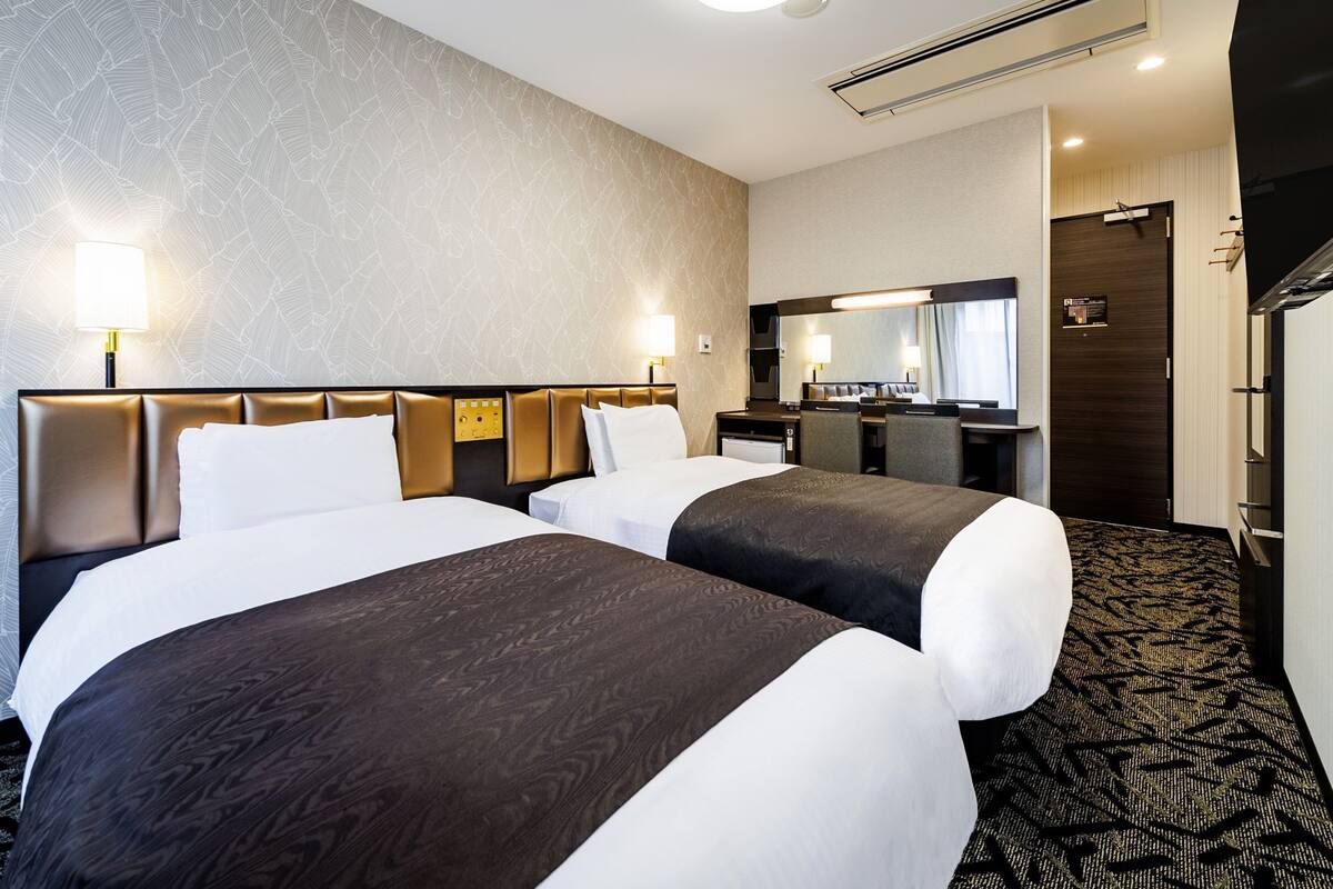 A hotel room with two beds, a desk, a mirror, and a bathroom door.