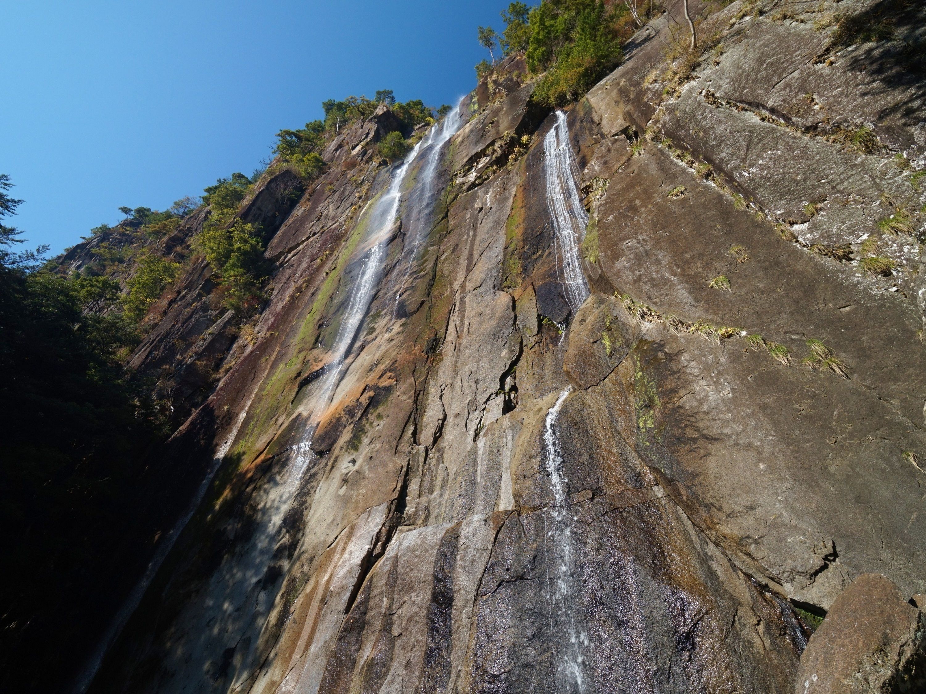 Una cascada de varios niveles desciende por un risco rocoso con vegetación escasa.