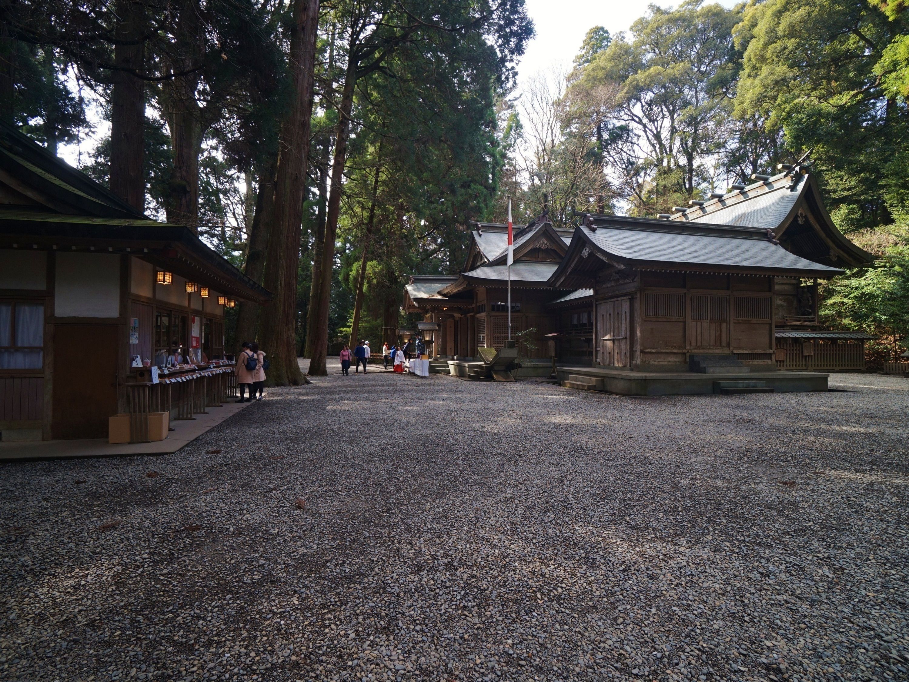 A traditional Japanese temple with a gravel courtyard, wooden buildings, and large trees.