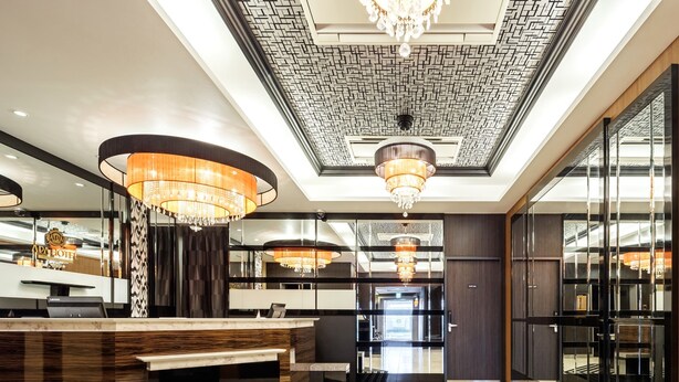 A modern hotel lobby with a reception desk, chandeliers, and a patterned ceiling. - APA Hotel Miyazaki Nobeoka Chuo (Nobeoka)
