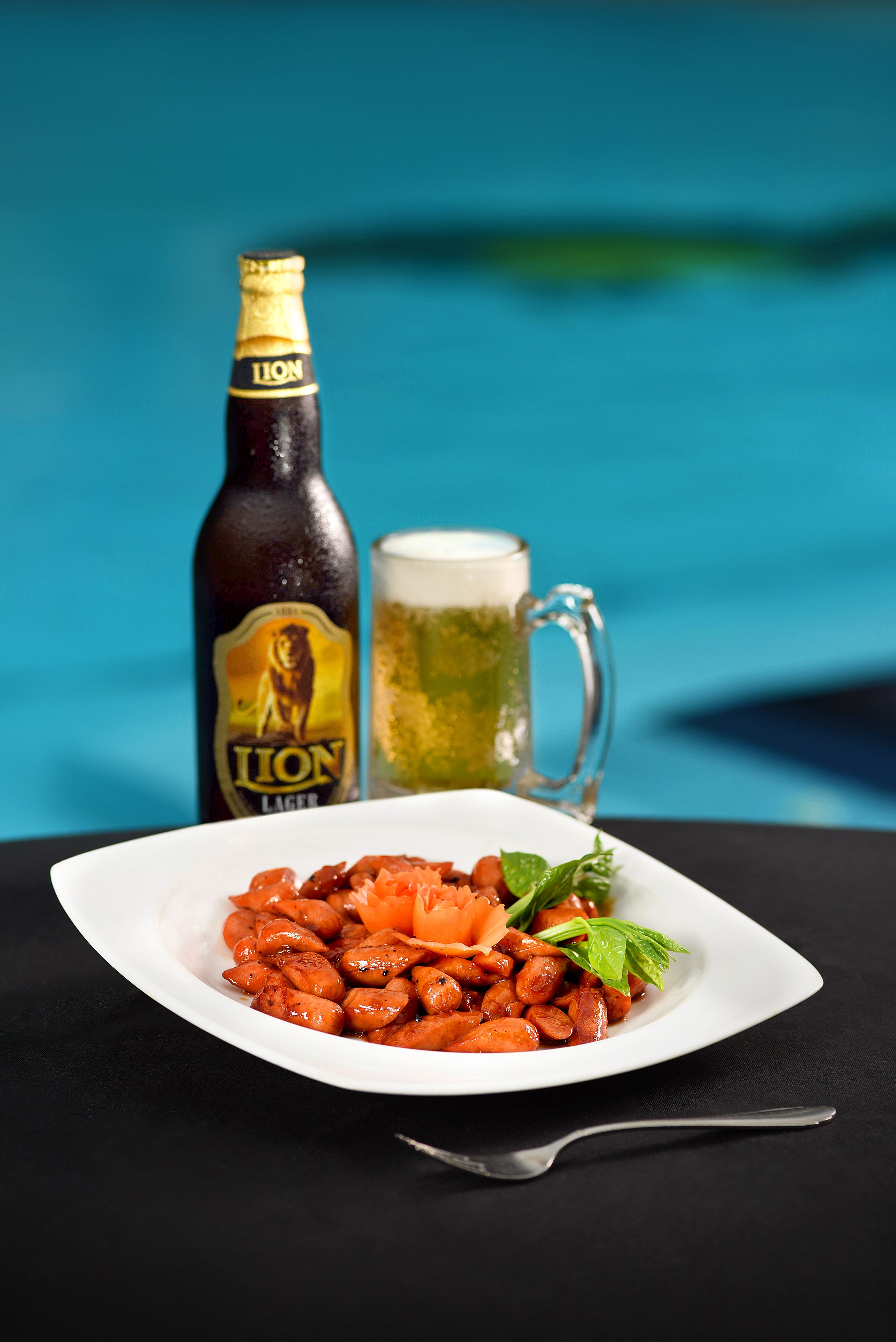A bottle of Lion Lager, a glass of beer, and a plate of roasted vegetables.