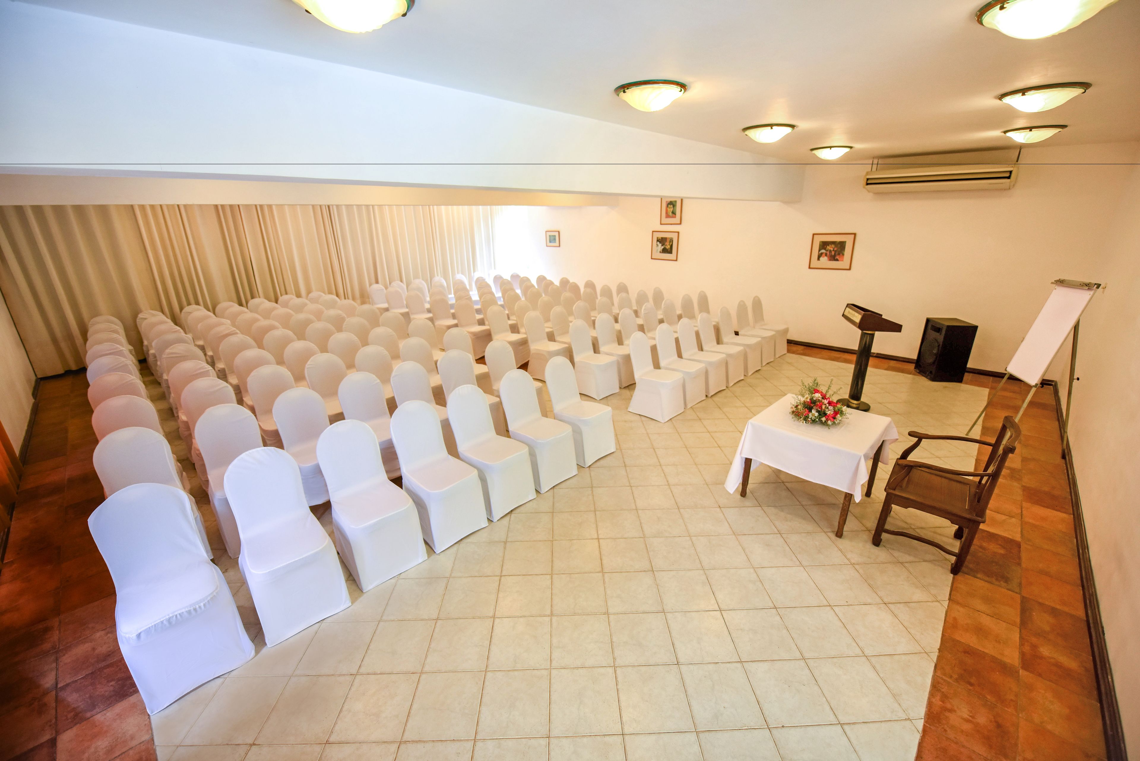 A conference room with rows of white chairs, a podium, and a white table with a floral arrangement.