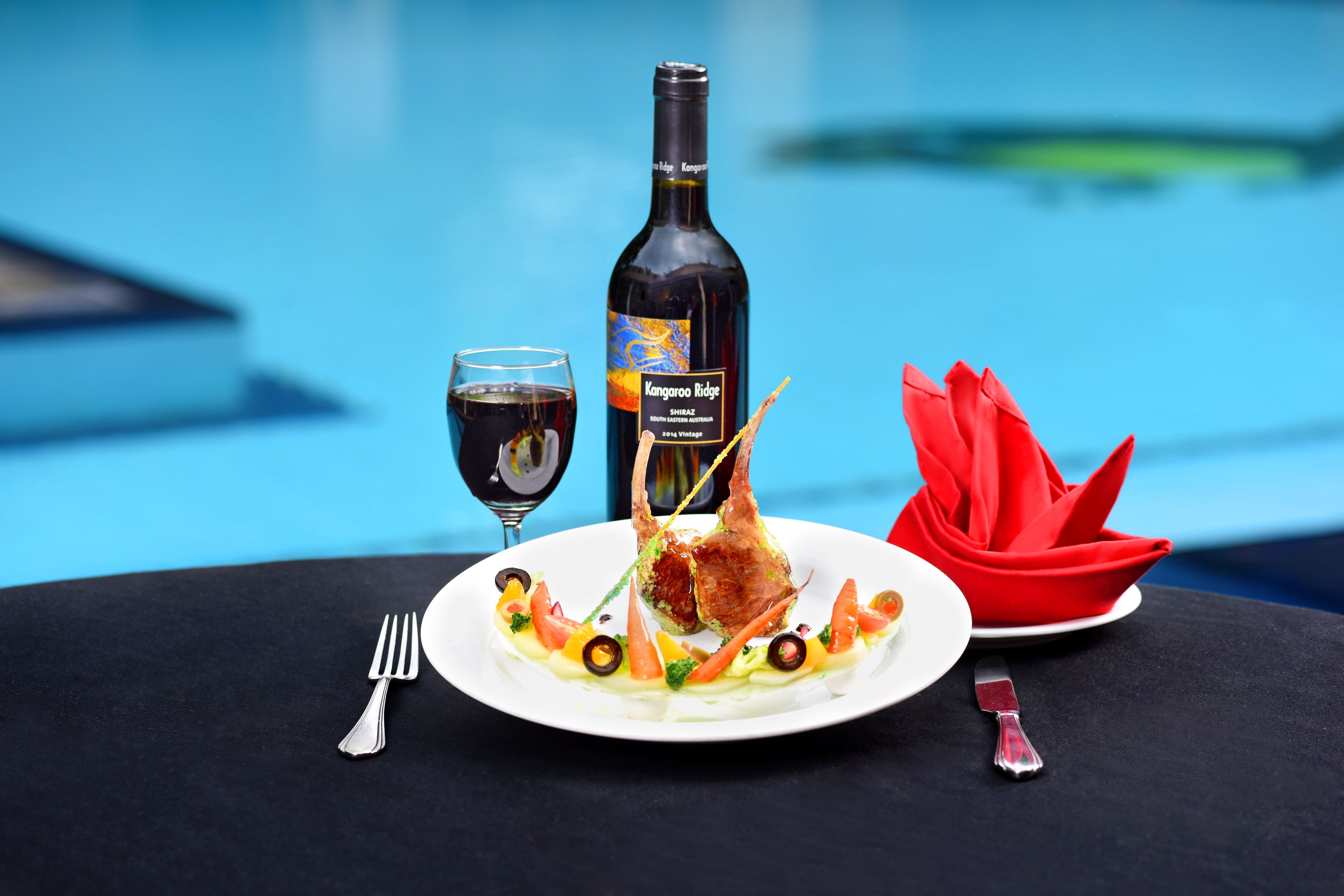 A dining table with a plate of food, a bottle of wine, and a glass of wine.