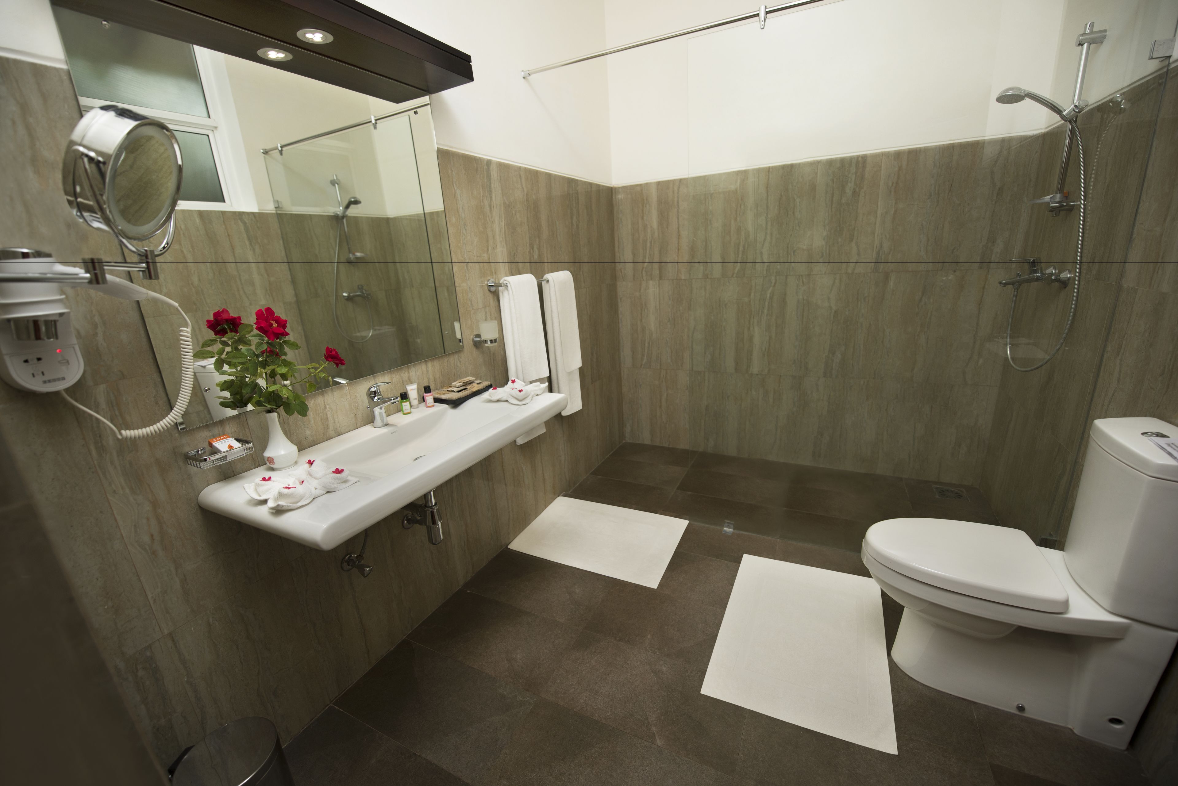 Un baño moderno con un espejo grande, un lavamanos, un inodoro y una zona de ducha.